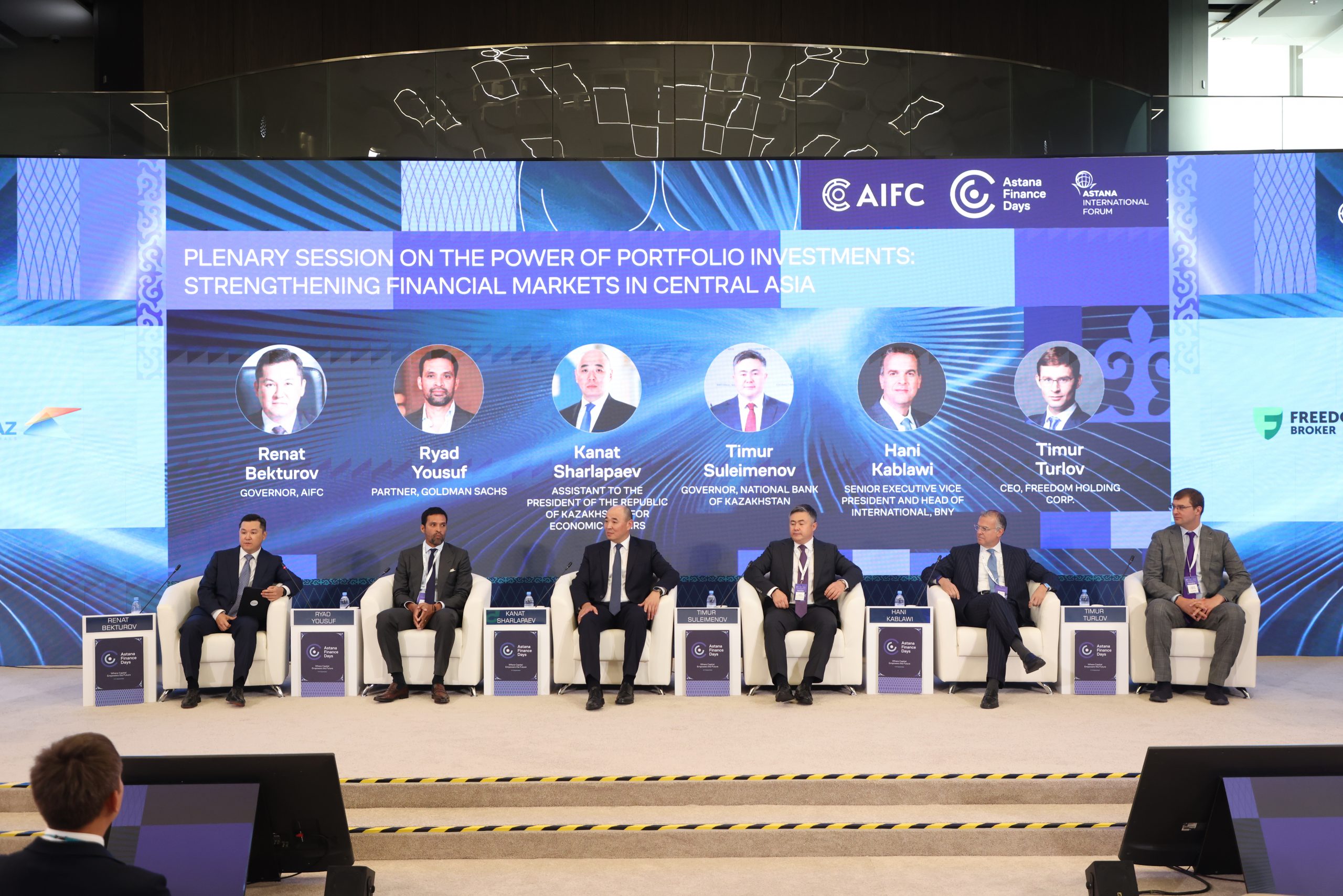 A wide-angle photograph of a plenary session at the Astana Finance Days conference, titled "Plenary Session on the Power of Portfolio Investments: Strengthening Financial Markets in Central Asia." Six men, including Renat Bekturov, Ryad Yousuf, Kanat Sharlapaev, Timur Suleimenov, Hani Kablawi, and Timur Turlov, are seated in armchairs on a stage in front of a large screen with the event's branding and their names.